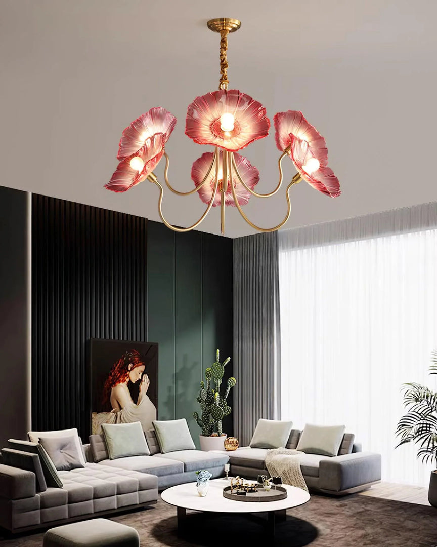 A captivating Oleander Floral Chandelier with vibrant pink glass petal shades and a gold frame hanging above a chic modern living room, featuring a gray sectional sofa with white and pastel cushions, a round marble coffee table, and bold accent decor, including a vertical slat panel wall and contemporary artwork.