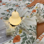 Load image into Gallery viewer, Softly glowing pear-shaped bedside lamp placed on floral-patterned bedding, surrounded by cozy accents, including a bubble candle and an open book for a serene bedroom ambiance.
