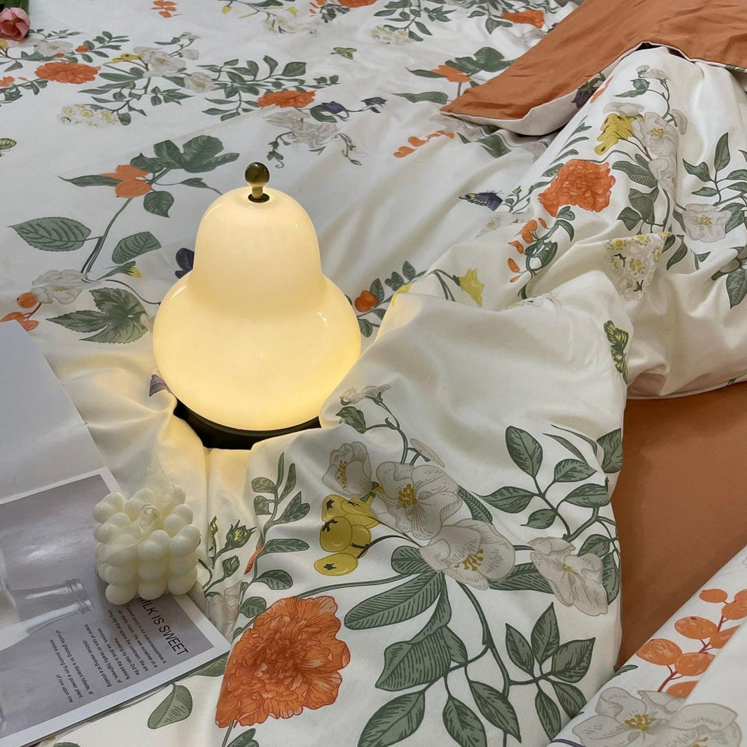 Softly glowing pear-shaped bedside lamp placed on floral-patterned bedding, surrounded by cozy accents, including a bubble candle and an open book for a serene bedroom ambiance.