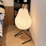 Load image into Gallery viewer, Minimalist pear-shaped floor lamp with a soft glowing white shade and black frame, placed beside a cozy bed and a modern bookshelf.
