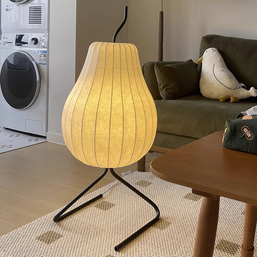 Cozy living room setting featuring a pear-shaped floor lamp with a glowing white shade, black metal stand, green sofa, and wooden coffee table.