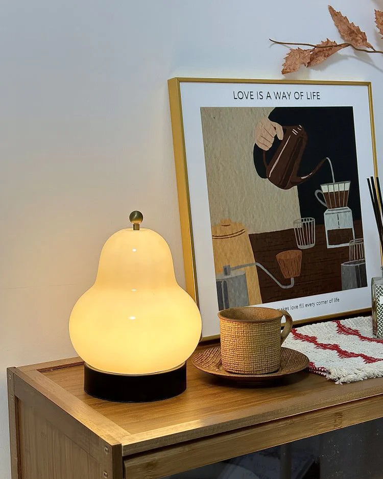 A cozy scene featuring a pear-shaped glass table lamp on a wooden dresser, softly illuminating a framed art piece and a ceramic mug for a warm ambiance.