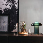 Load image into Gallery viewer, Persian green table lamp placed on a dark wooden shelf, styled alongside glass vases, a terrarium dome with plants, and modern monochrome artwork for a chic decorative setup.
