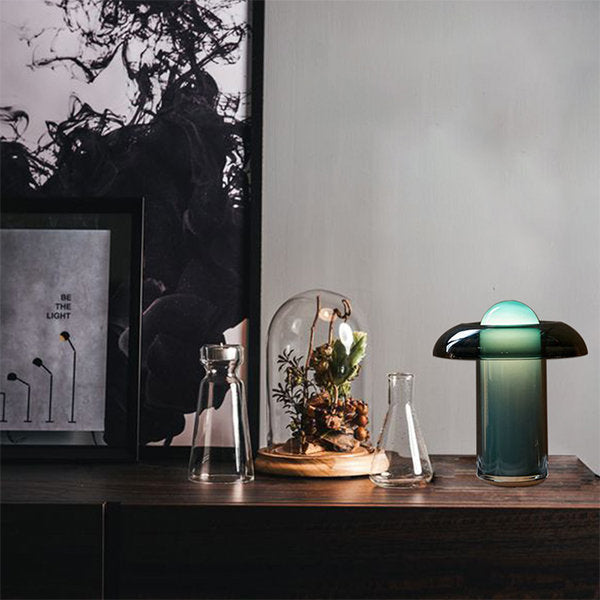 Persian green table lamp placed on a dark wooden shelf, styled alongside glass vases, a terrarium dome with plants, and modern monochrome artwork for a chic decorative setup.