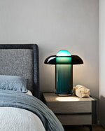 Load image into Gallery viewer, Persian green table lamp glowing softly on a modern wooden nightstand, styled with cozy folded linens and paired with a gray upholstered headboard in a serene bedroom setting.
