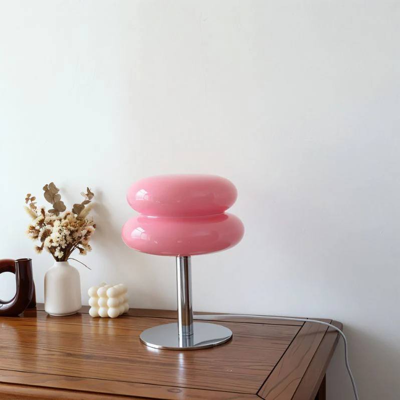 Elegant pink glossy macaron table lamp displayed on a wooden table, complemented by a serene home decor setup with dried flowers and minimalist accessories.