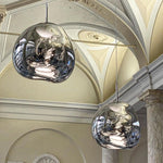 Load image into Gallery viewer, A classical interior featuring two rock pendant lamps with reflective silver surfaces hanging from an ornate ceiling with arches and intricate detailing, complemented by tall marble columns.
