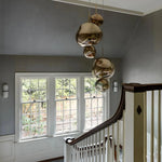 Load image into Gallery viewer, An elegant stairwell featuring a cluster of rock pendant lamps with gold reflective surfaces, hanging in front of large colonial-style windows that offer a view of the garden, complemented by soft gray walls and white wainscoting.
