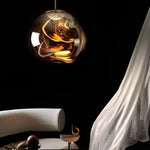 Load image into Gallery viewer, A luxurious ambiance featuring a rock pendant lamp with warm reflective gold tones, paired with a curved white chair, a cocktail glass on a sleek black table, and flowing sheer curtains against a dramatic dark background.
