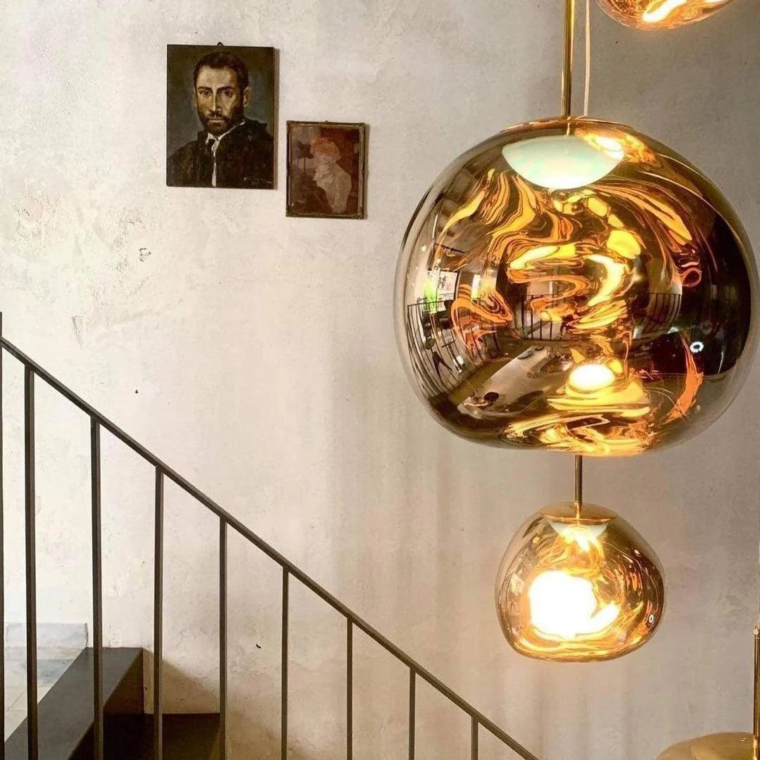 A modern staircase with a rock pendant lamp featuring reflective gold surfaces, casting warm ambient light, complemented by minimal wall decor with two vintage portraits on a textured wall.