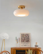 Load image into Gallery viewer, A cozy room featuring the Sanna cylinder ceiling light with a white shade and brass mount, paired with a wooden sideboard decorated with a William Morris art print, colorful candlesticks, and a decorative vase, creating an artistic and elegant ambiance.
