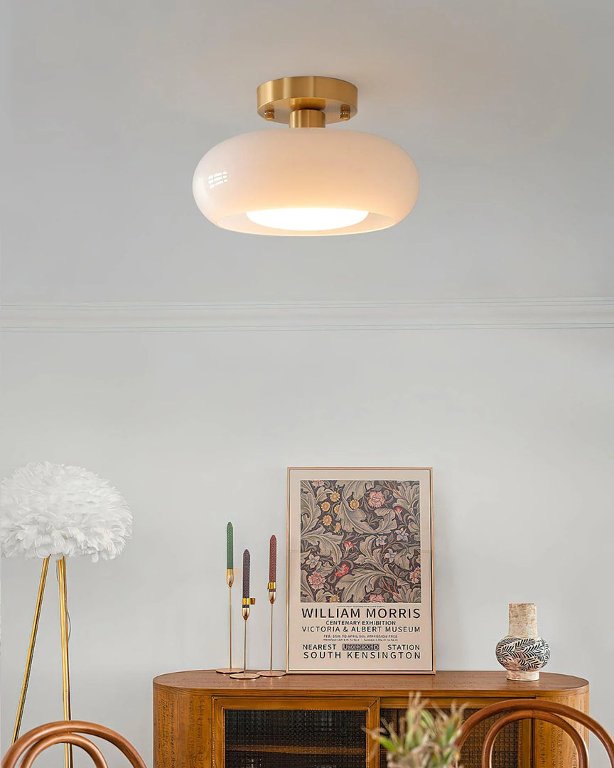 A cozy room featuring the Sanna cylinder ceiling light with a white shade and brass mount, paired with a wooden sideboard decorated with a William Morris art print, colorful candlesticks, and a decorative vase, creating an artistic and elegant ambiance.