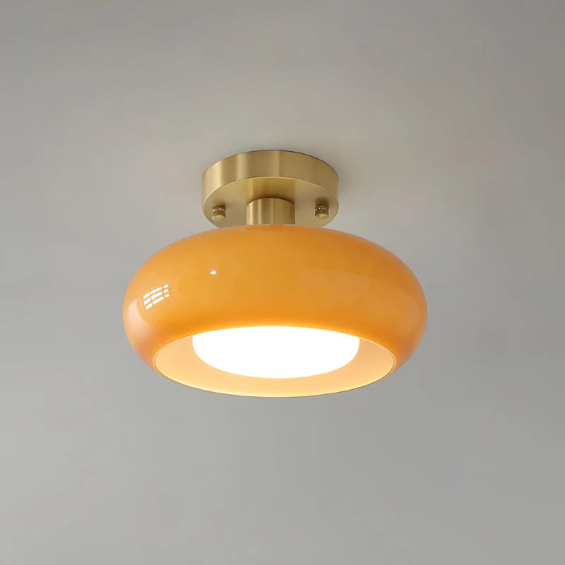 A sleek Sanna cylinder ceiling light with a warm amber shade and a brushed brass mount, providing soft and ambient illumination, ideal for contemporary interiors.