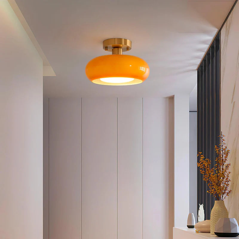 A modern hallway illuminated by the Sanna cylinder ceiling light featuring a warm amber shade and brass fixture, with minimal decor including vases and a textured wall accent for a clean and elegant ambiance.