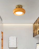 Load image into Gallery viewer, A contemporary study room illuminated by the Sanna cylinder ceiling light with a warm amber shade and brass mount, featuring a minimalist design with built-in shelving, a desk, and an arched mirror on a clean white wall.
