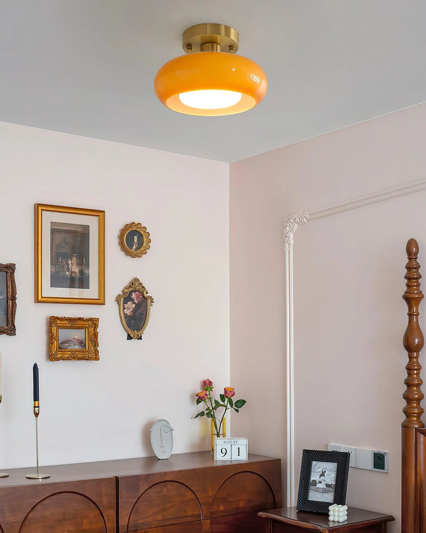 A vintage-inspired bedroom featuring the Sanna cylinder ceiling light with a warm amber shade and brass fixture, complemented by a gallery wall of ornate picture frames, a wooden dresser adorned with decor, and a classic four-poster bed.