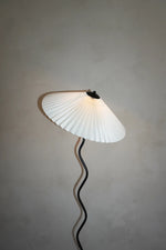 Load image into Gallery viewer, A closeup view of the Seashell floor lamp showcasing its pleated white shade and sculptural wavy stand, set against a neutral wall, highlighting its elegant and modern design.
