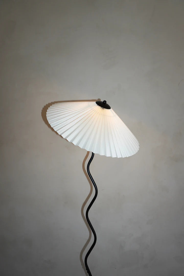 A closeup view of the Seashell floor lamp showcasing its pleated white shade and sculptural wavy stand, set against a neutral wall, highlighting its elegant and modern design.