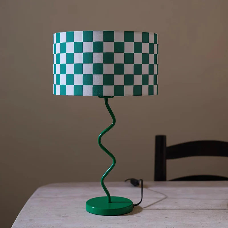 Showcasing the Spiraled Green Checker Lamp, this image presents a captivating green and white checkered lampshade mounted on an elegantly twisted green base. The lamp’s fresh, modern design and vibrant colors make it a distinctive accent piece, positioned on a plain table against a subtle backdrop, emphasizing its quirky and stylish character.