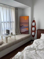 Load image into Gallery viewer, A Surfboard Floor Lamp with a sleek wooden design and glowing panels placed beside a cozy window seat with a laptop and coffee cup, a sunset painting leaning against the wall, and a neatly styled bed in a serene bedroom setting.
