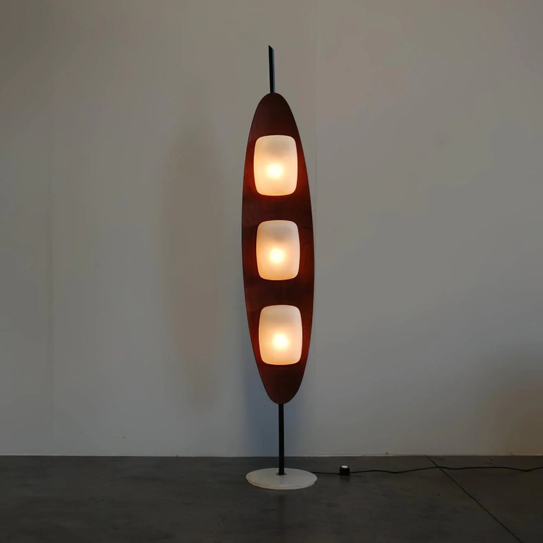 A Surfboard Floor Lamp featuring a sleek wooden frame with three glowing panels and a marble base, displayed against a plain wall, highlighting its modern and elegant design.