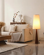 Load image into Gallery viewer, Stylish tapered floor lamp with wooden base and soft glowing shade showcased in neutral living room with cream sofa, geometric rug, and decorative accents including classical bust and dried botanicals
