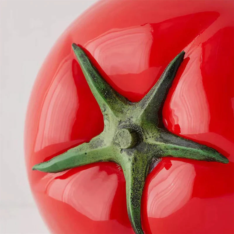 A close-up view of the glossy red surface and green stem detail of a tomato-shaped table lamp, showcasing its realistic texture and vibrant finish.