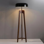 Load image into Gallery viewer, A modern floor lamp with a wooden tripod base and a black dome-shaped shade, emitting warm light against a neutral gray background, showcasing its clean and minimalist design.
