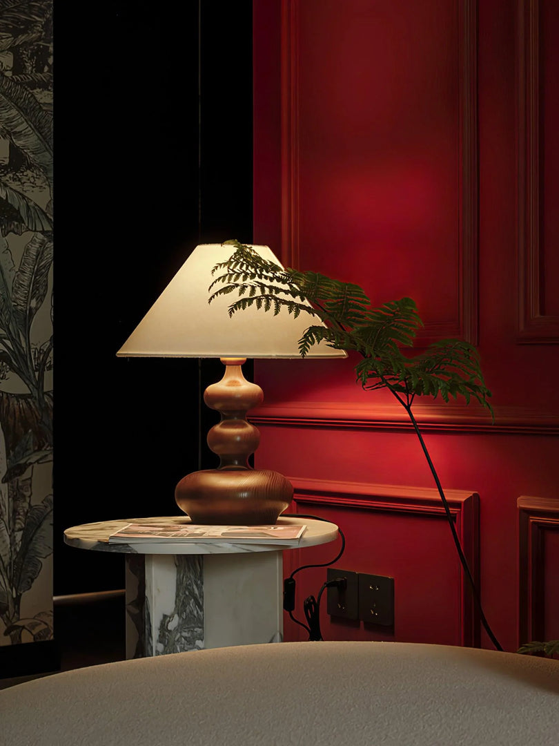 Rich and intimate atmosphere enhanced by a Vintage Gourd Water Bottle Lamp, with its sculptural base and traditional lampshade casting a warm glow beside a marble table. The deep red walls and a verdant potted plant add to the classic and cozy feel of this elegant corner.