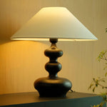 Load image into Gallery viewer, A close-up view of a Warm Wooden Gourd Table Lamp featuring a unique, sculptural base with flowing curves in a dark wood finish, topped with a large, bright white shade. The lamp casts a gentle glow, enhancing the warm ambiance against a soft-lit wooden backdrop, ideal for creating a cozy and inviting space.
