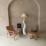 Load image into Gallery viewer, A wavy white floor lamp with a pleated shade, styled in a minimalist living room with an arched alcove, a leather chair, and a wooden coffee table featuring decorative accents.
