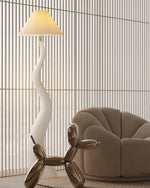 Load image into Gallery viewer, A wavy white floor lamp with a pleated shade, featured in a modern living space with vertical wooden slats, a sculptural beige armchair, and a metallic balloon dog decor piece.
