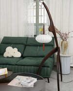 Load image into Gallery viewer, The wooden mantis floor lamp in a cozy living room with a green sofa, a cloud-shaped pillow, a round coffee table, and a vase with decorative flowers near a window.
