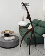 Load image into Gallery viewer, The wooden mantis floor lamp in a contemporary living room with a green sofa, a circular coffee table, and modern wall art, creating a stylish and functional decor element.
