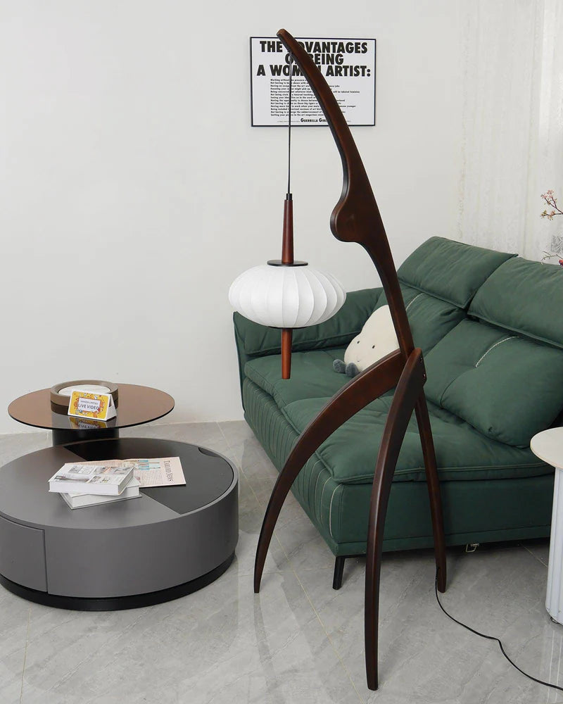 The wooden mantis floor lamp in a contemporary living room with a green sofa, a circular coffee table, and modern wall art, creating a stylish and functional decor element.