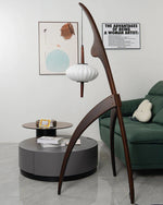 Load image into Gallery viewer, The wooden mantis floor lamp in a modern living room with a green sofa, a round coffee table, and abstract wall art, blending contemporary style with unique design.
