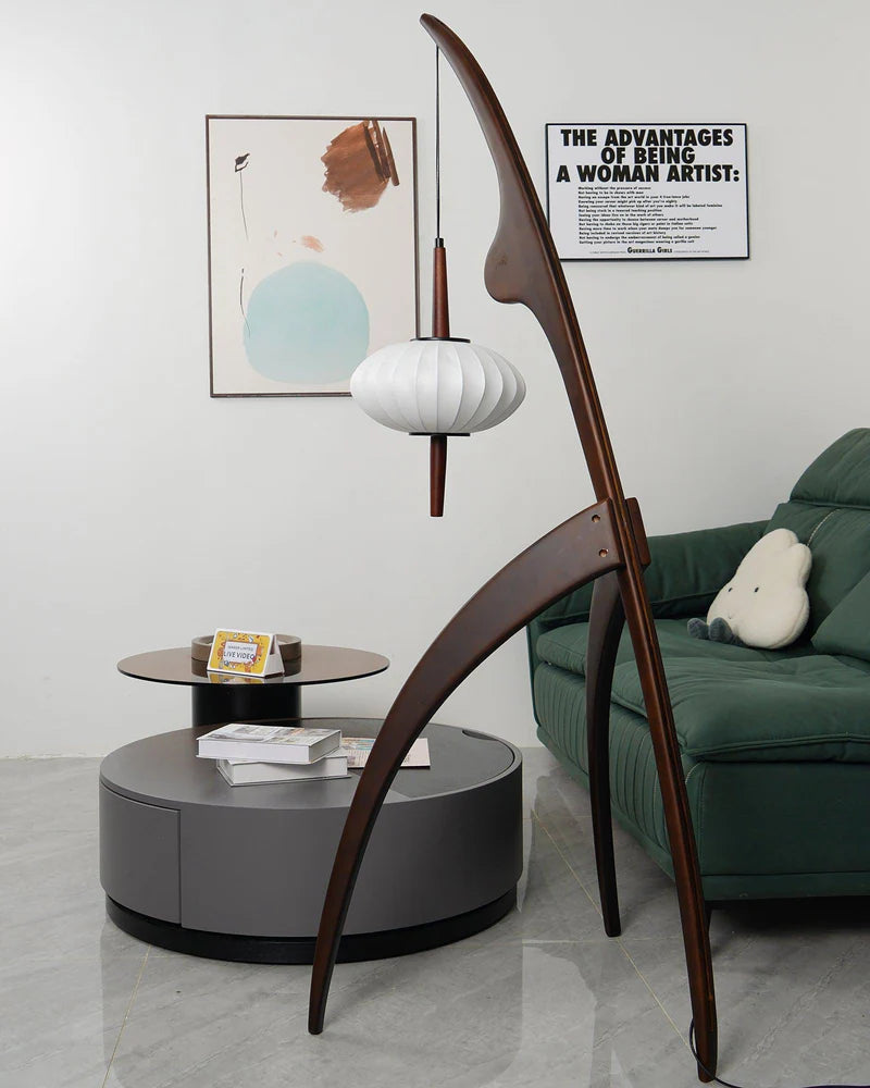 The wooden mantis floor lamp in a modern living room with a green sofa, a round coffee table, and abstract wall art, blending contemporary style with unique design.